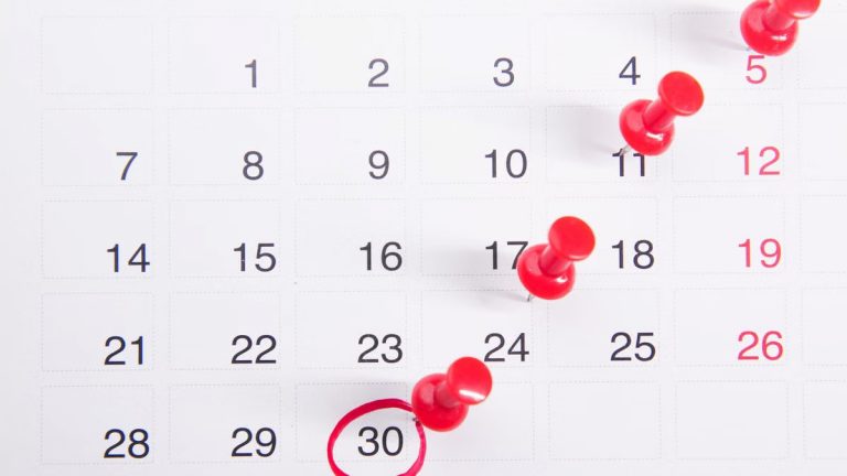 Close-up of a calendar with red push pins marking important dates, emphasizing deadlines.