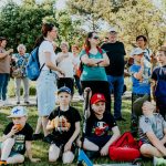 A diverse group of families and children enjoying an outdoor event on a sunny day in a park setting.