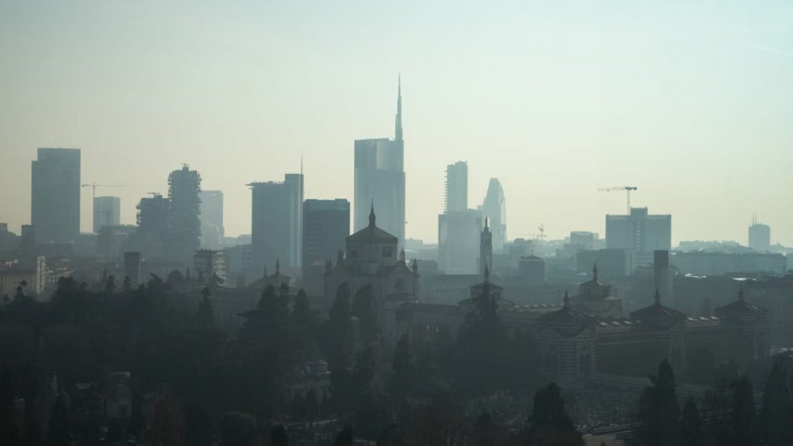 A foggy view of the Milan cityscape with modern skyscrapers and historic architecture.