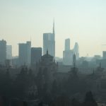 A foggy view of the Milan cityscape with modern skyscrapers and historic architecture.